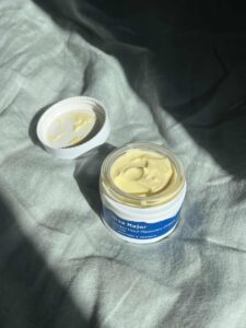Open cream jars with natural homemade moisturiser on a grey linen background
