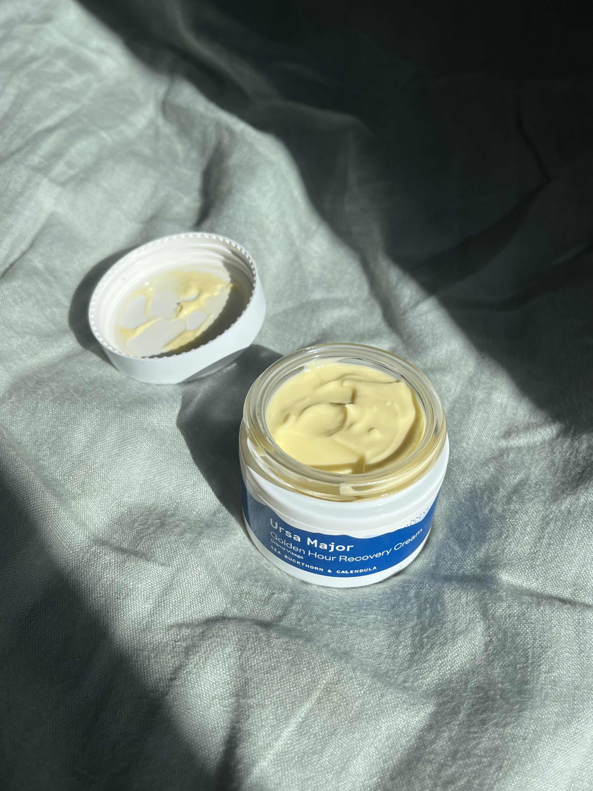 Open cream jars with natural homemade moisturiser on a grey linen background
