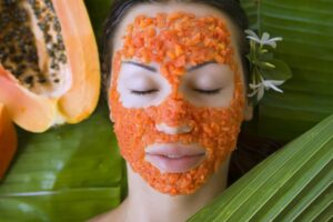 Woman with papaya enzyme face mask on tropical green leaves