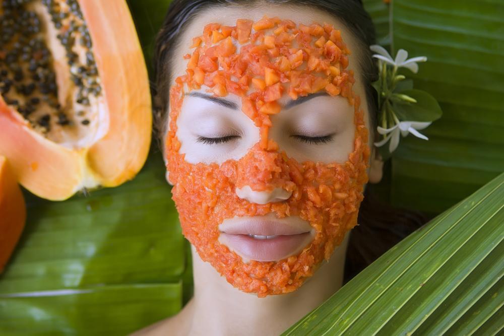 Woman with papaya enzyme face mask on tropical green leaves